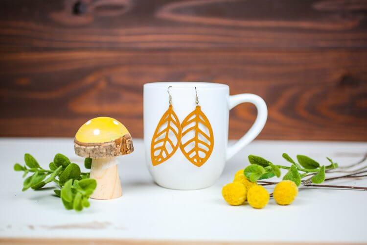 A mushroom figurine next to yellow floral sprig and a coffee mug that has a pair of earrings hanging from it