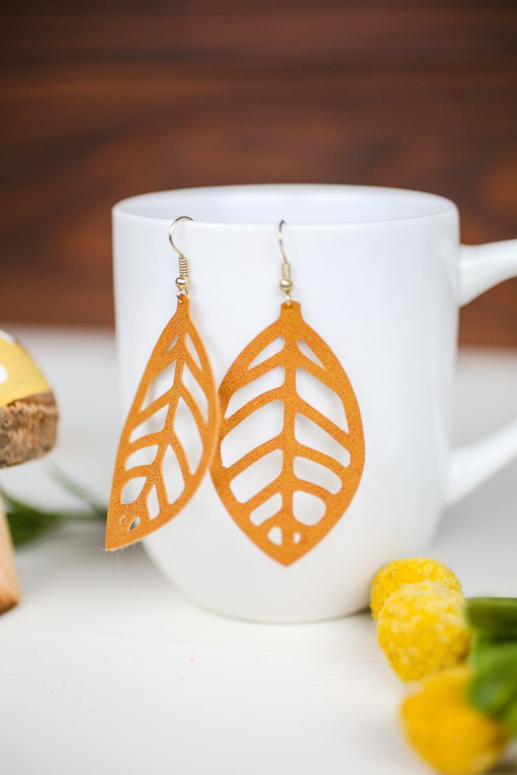 A close up of a mushroom figurine next to yellow floral sprig and a coffee mug that has a pair of earrings hanging from it