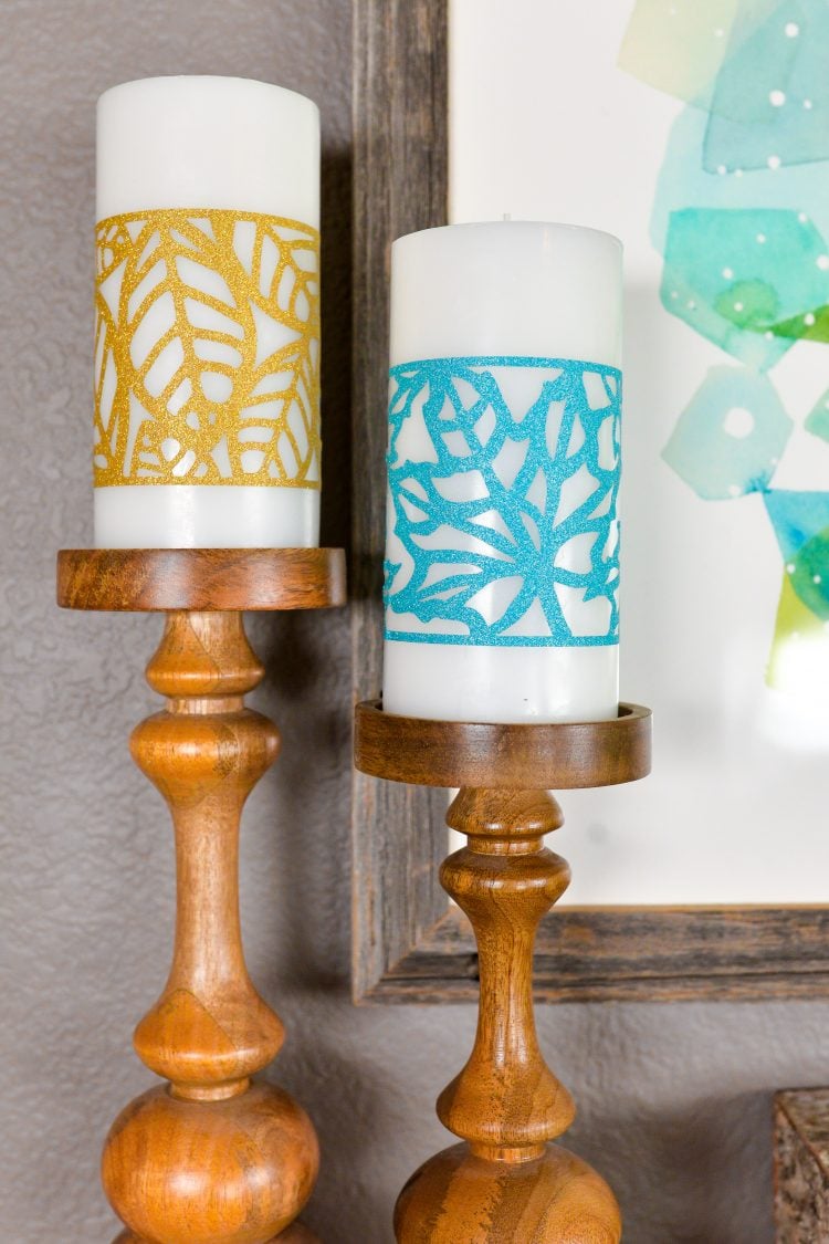 Two white candles in wooden candle holders and decorated with an aqua and a gold fall leave wrap sitting next to a picture in a wooden frame