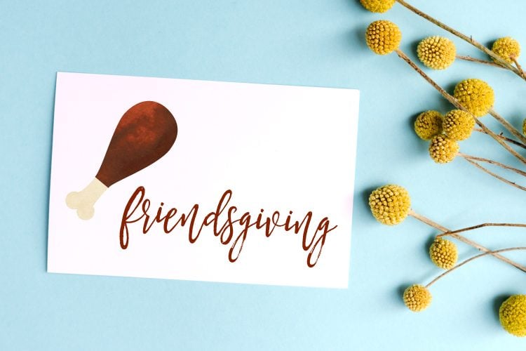 A spray of gold flowers lying next to a piece of paper that contains an image of a drumstick and the word \"Friendsgiving\"