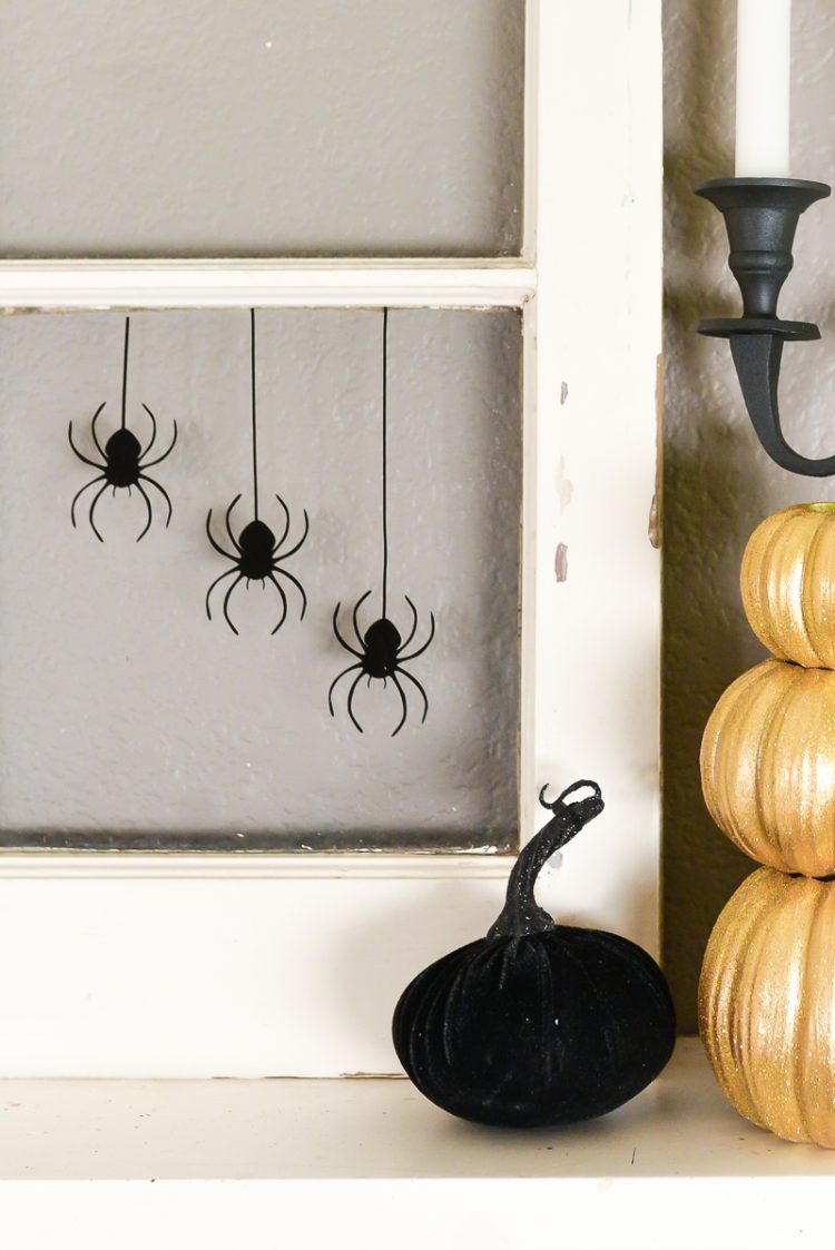 Close up of an old window decorated with a black spider web and spiders sitting on top of a fireplace mantel and next to candles and pumpkins