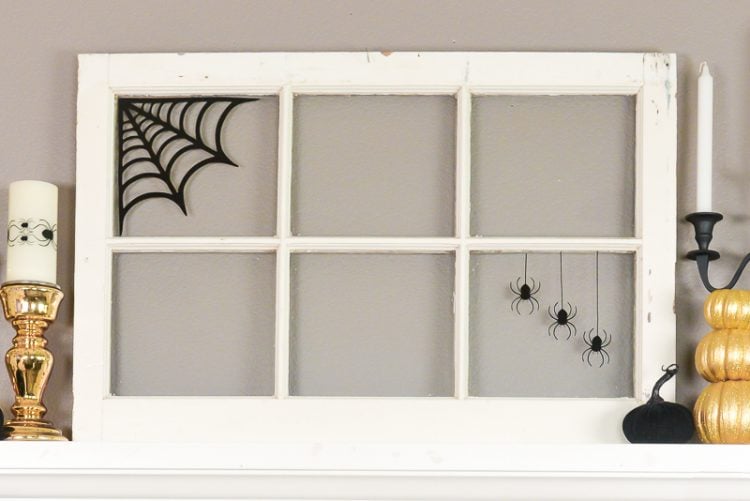 An old window decorated with a black spider web and spiders sitting on top of a fireplace mantel and next to candles and pumpkins