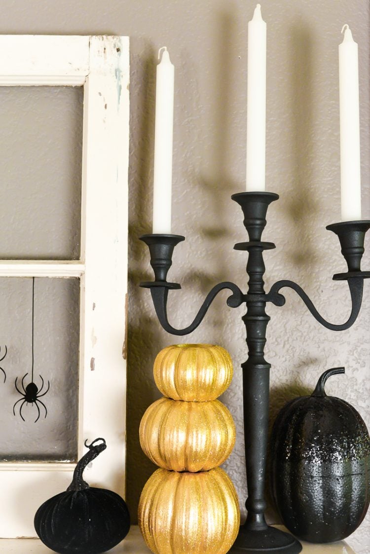 Close up of an old window sitting next to gold and black pumpkins and white candles in a black candelabra