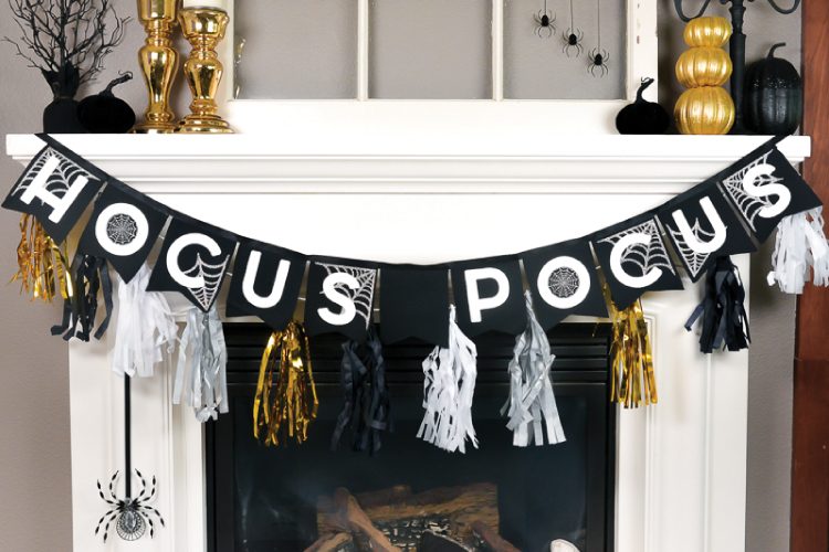 Halloween black, white and gold decor adorning a white fireplace that includes, gold and black pumpkins, white candles in black candelabras and a banner that says, \"Hocus Pocus\"