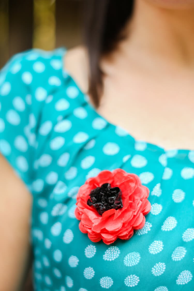 A close up of a woman in a blue polka dotted shirt with a paper poppy pinned to it