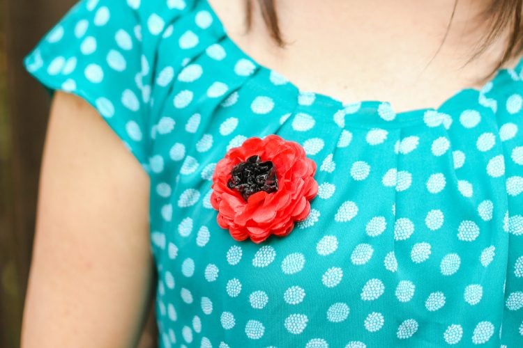 A close up of a woman in a blue polka dotted shirt with a paper poppy pinned to it