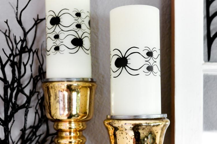 A close up of two gold candlesticks with white candles decorated with images of spiders