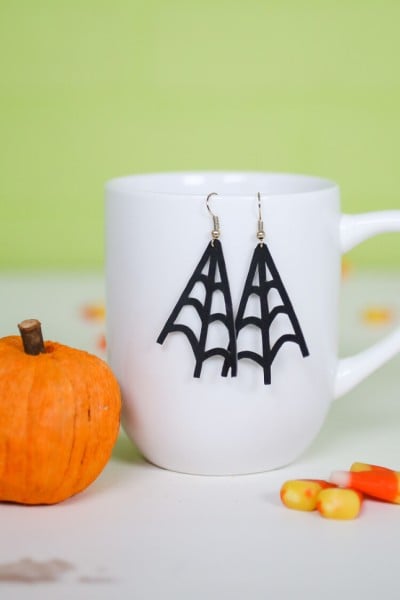 On a table sits a small pumpkin, some candy corn candy and a coffee mug with earrings hanging from it