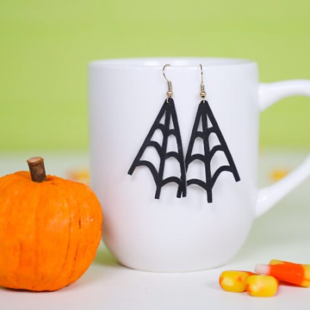 On a table sits a small pumpkin, some candy corn candy and a coffee mug with earrings hanging from it