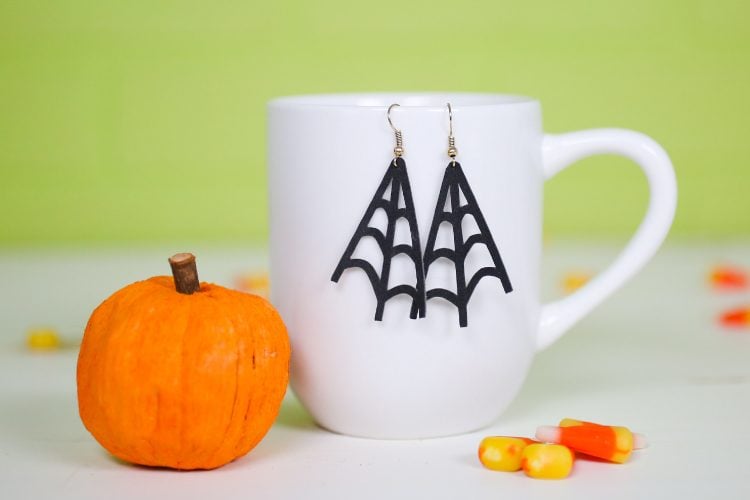 On a table sits a small pumpkin, some candy corn candy and a coffee mug with earrings hanging from it