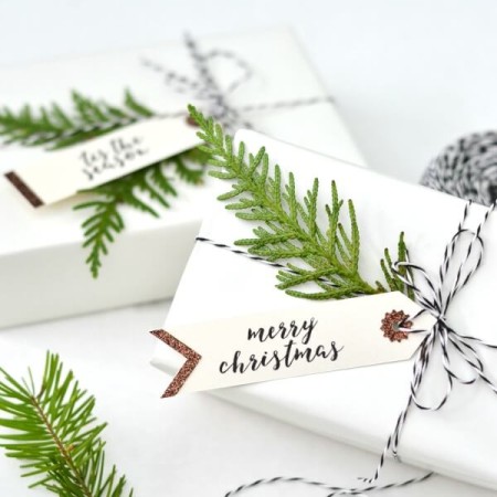 Gifts wrapped in white papers with greenery and gift tags attached