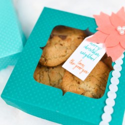 An aqua colored polka dot box filled with cookies and decorated with a coral colored felt poinsettia and a gift tag