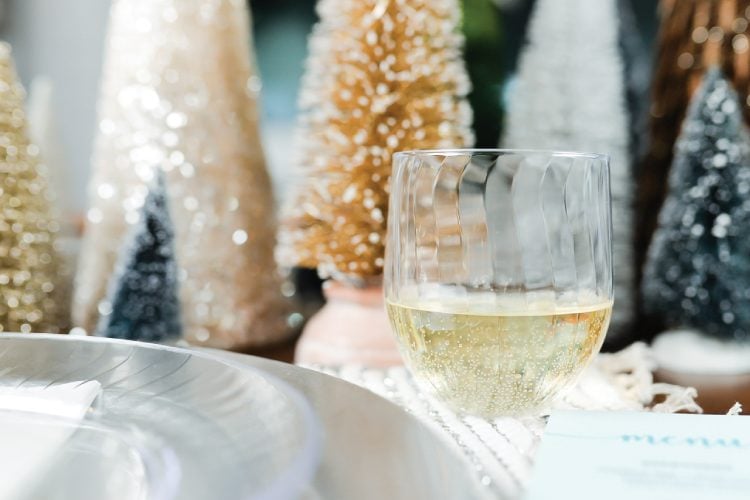 A glass of wine next to a table setting with glittery trees in the background