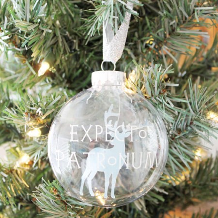 A glass ornament hanging from a Christmas tree, and is decorated with an image of a deer and says, "Expecto Patronum"