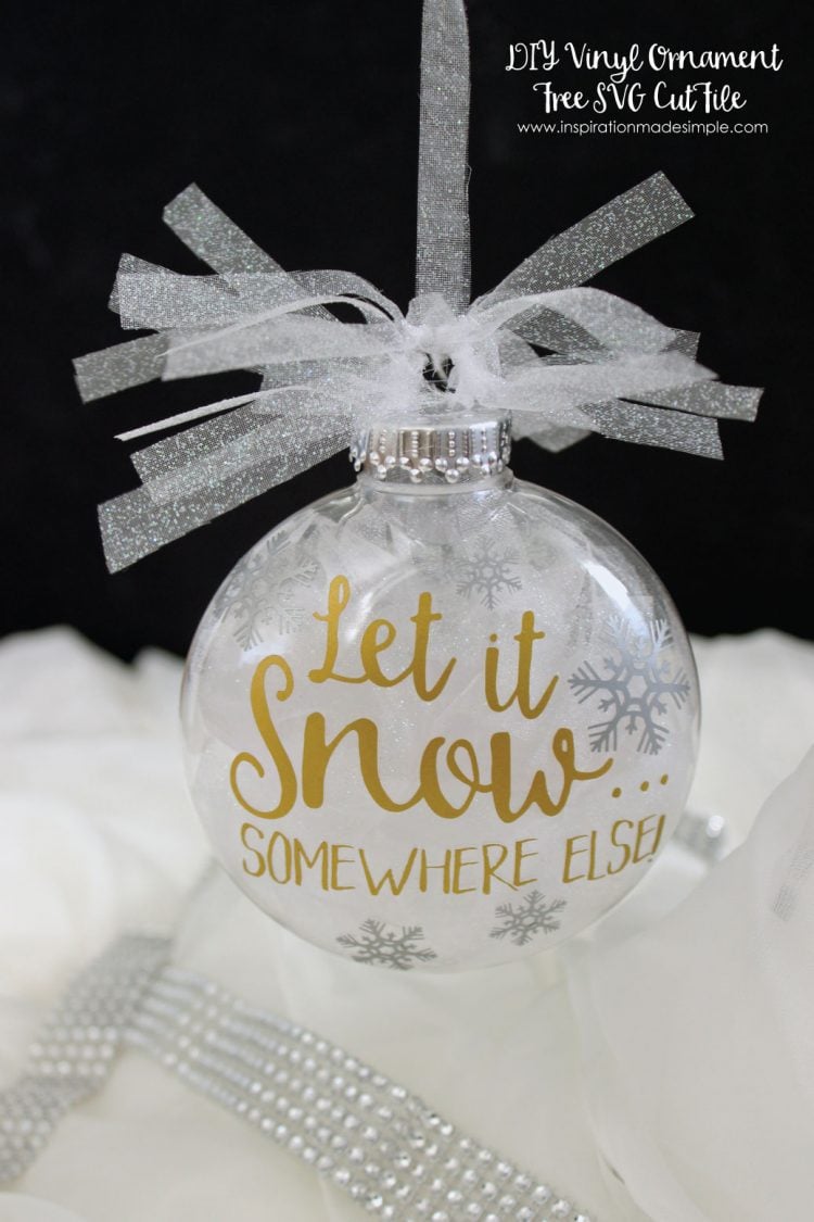 A close up of a glass ornament hanging from some sparkly ribbon, and says, \"Let it Snow Somewhere Else\"