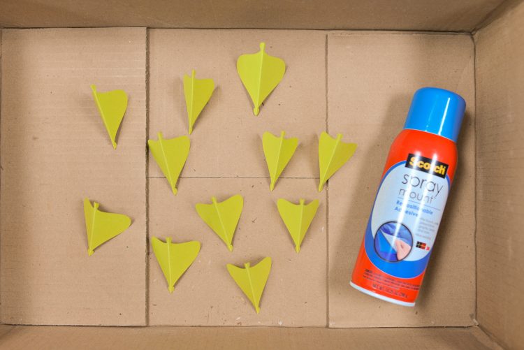 Pieces of paper ornament and a can of spray adhesive inside of a cardboard box