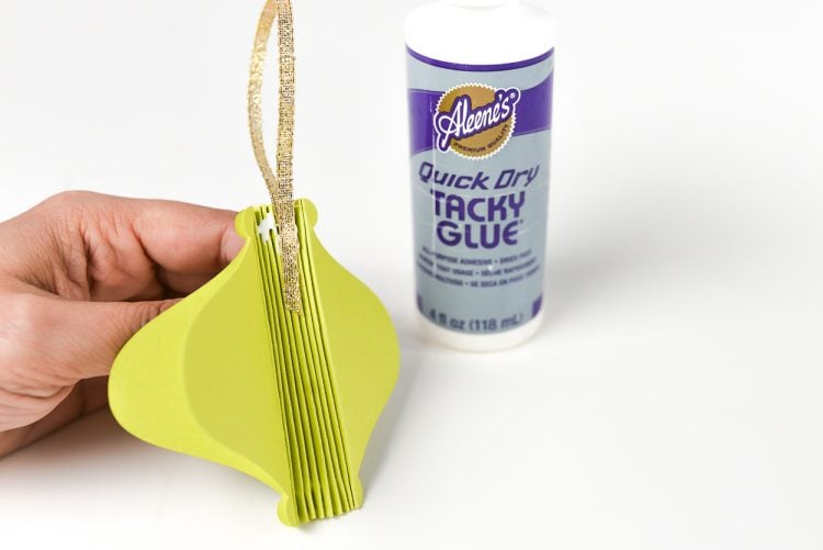 A hand holding a partially assembled paper ornament next to a bottle of tacky glue