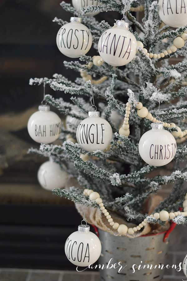 Small white ornaments hanging from a small tree and each ornament has one word on it such as, \"Frosty\", \"Christmas\", \"Jingle\", \"Bah Humbug\" and Santa