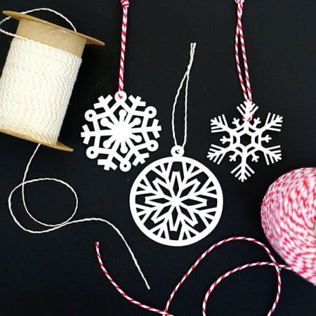 Spools of white string and red and white striped string next to paper snowflake ornaments