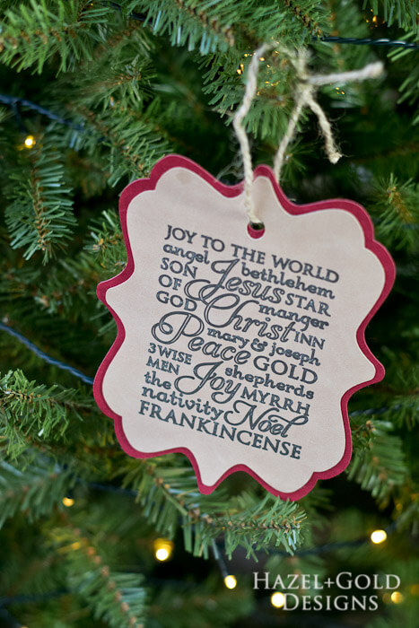 A close up of a Christmas tree with a paper cut ornament hanging from it filled with words of Christmas