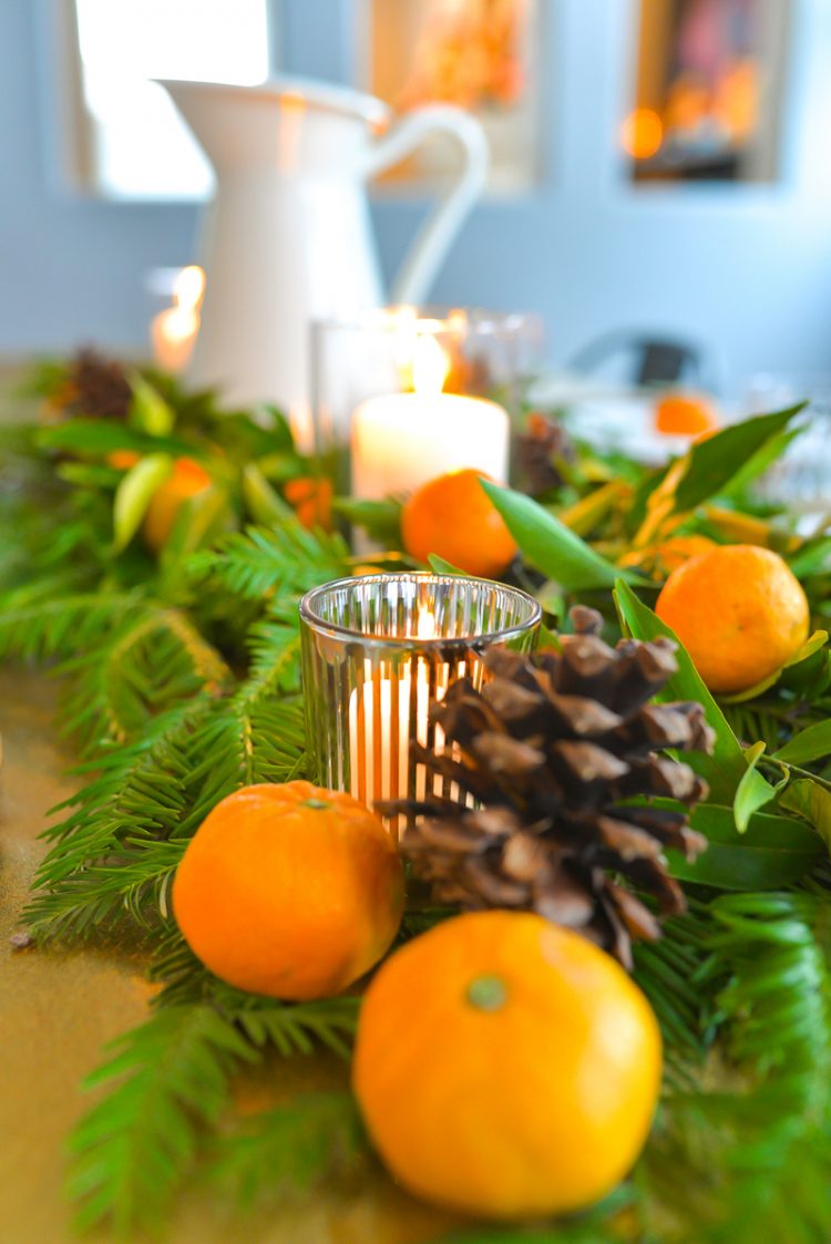 A close-up image of a table decorated with greenery, a candle and oranges