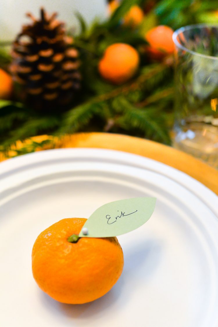 Close up of a plate with an orange on it and a paper leaf attached to the orange with a personalized name on it