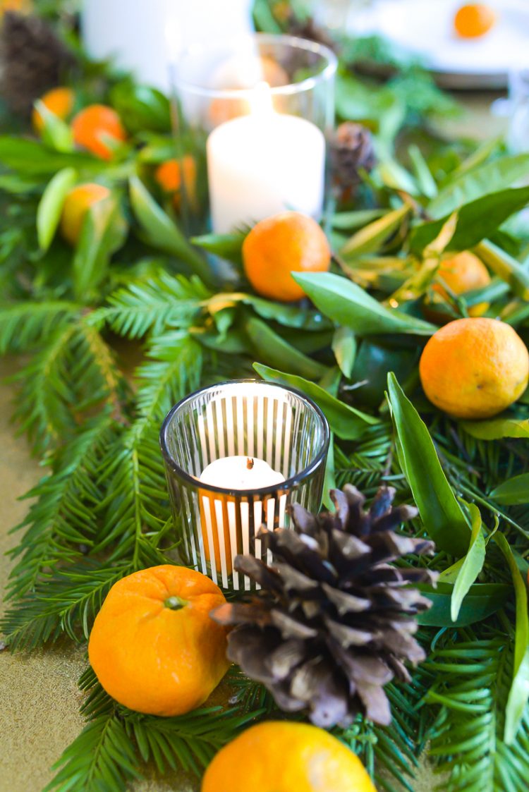 A close-up image of a table decorated with greenery, candles and oranges