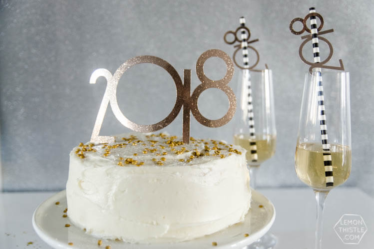 Champagne flutes with straws decorated with the year 2018 on them and a white cake on a table with a cake topper that has the year 2018