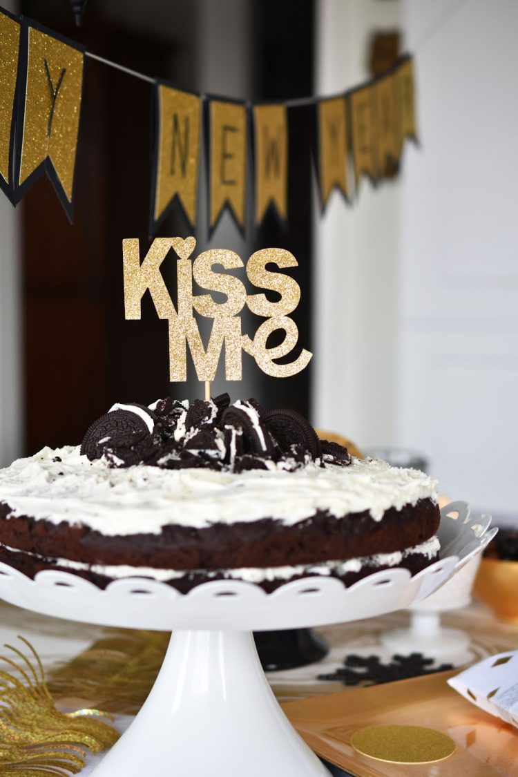 A cake sitting on top of a table with a cake topper that says, \"Kiss Me\"