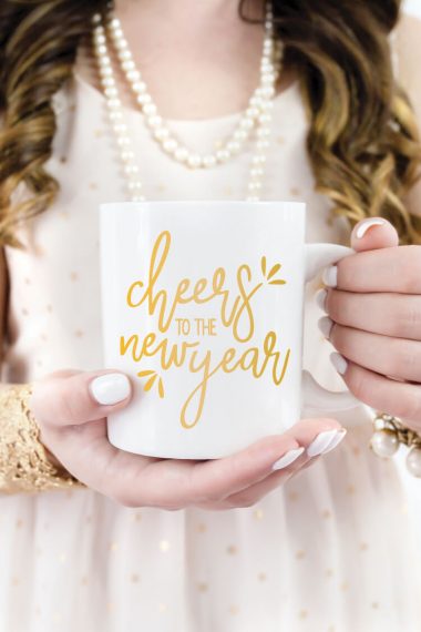 A woman holding a coffee mug with the words "Cheers to the New Year" on it