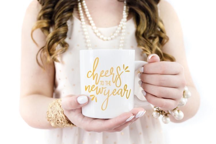A woman holding a coffee mug with the words \"Cheers to the New Year\" on it