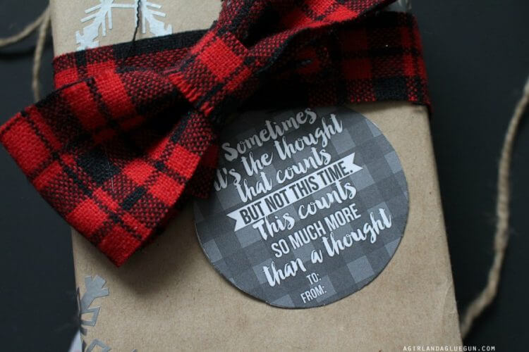 Close up of a package wrapped in a buffalo plaid bow and has a gift tag on it that says, \"Sometimes it\'s the thought that counts, but not this time. This counts so much more that a thought\".