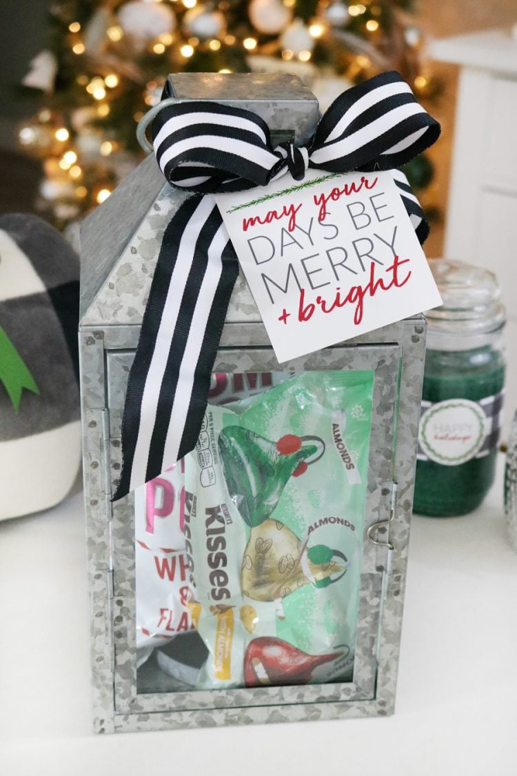 A tin lantern filled with candy and decorated with a black and white striped bow and a Christmas gift tag that says, \"My You Days Be Merry & Bright\"