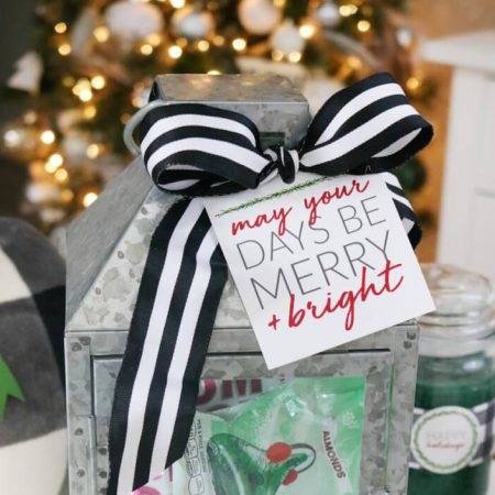 A tin lantern filled with candy and decorated with a black and white striped bow and a Christmas gift tag that says, "My You Days Be Merry & Bright"