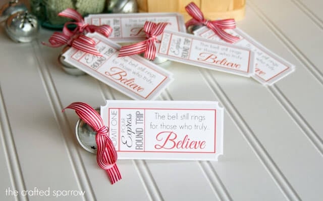 Close up of Christmas gift tags with a red bow and a jingle bell tied to each and they say, \"Admit One - Polar Express Round Trip - The bell still rings for those who truly believe\"