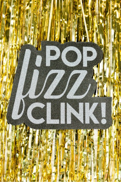 A sign that says, "Pop Fizz Clink!" hanging from a background of gold tinsel