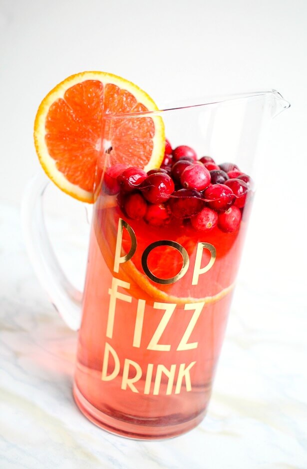 A glass filled with a beverage with cherries on top and an orange slice with the saying, \"Pop Fizz Drink\" on the side of the glass