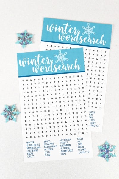 Decorative snowflakes lying next to two Winter Wordsearch papers
