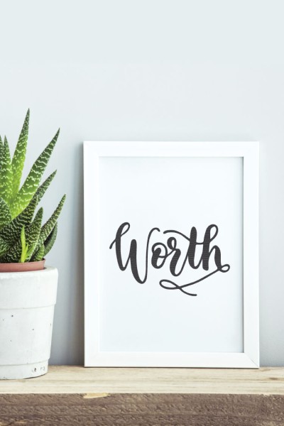 A plant sitting on a table next to a sign with a white frame and the sign says, "Worth"
