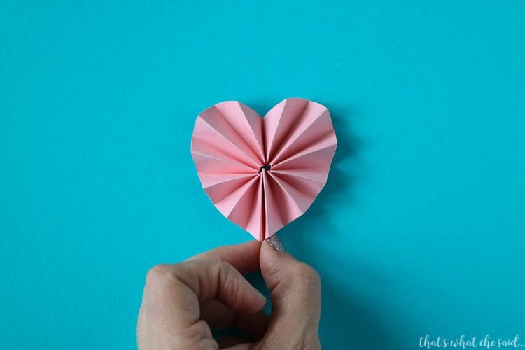 A hand holding a piece of accordion folded paper that is in the shape of a heart