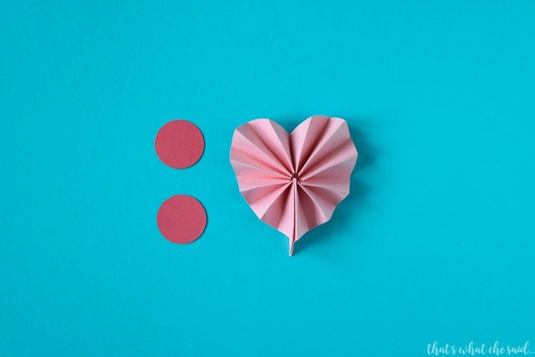 A piece of accordion folded paper that is in the shape of a heart and two pink dots