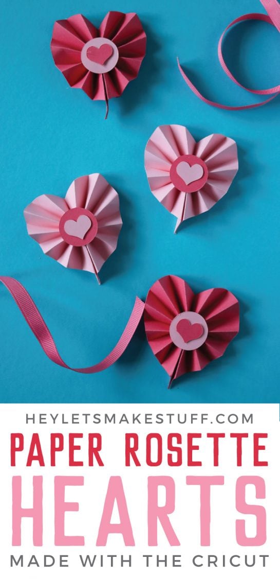 Accordion folded paper hearts with a pink dot on top of each one and a small pink heart on top of the dot on each one and ribbon attached to each for hanging them along with advertising from HEYLETSMAKESTUFF.COM for Paper Rosette Hearts Made with the Cricut
