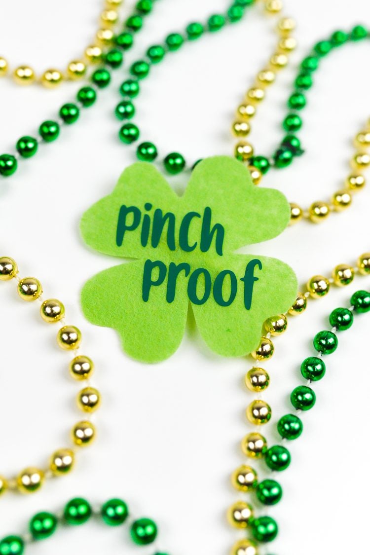 A close up of Gold and green colored beads on a table next to a green shamrock that says, \"Pinch Proof\"