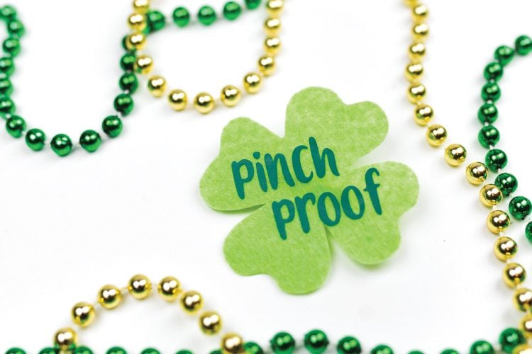 Gold and green colored beads on a table next to a green shamrock that says, \"Pinch Proof\"