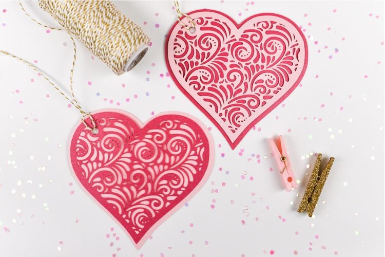 A close up of a roll of twine and two small clothespins next to two hearts cut out of paper