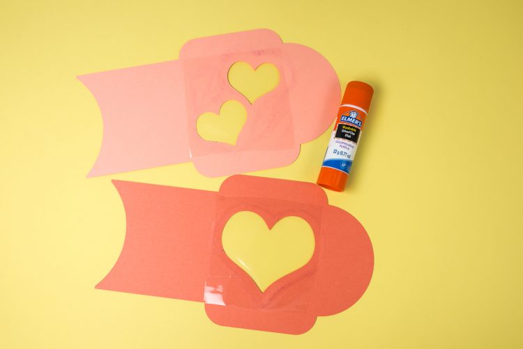 Two pieces of paper with cutout hearts and a stick of Elmer\'s glue