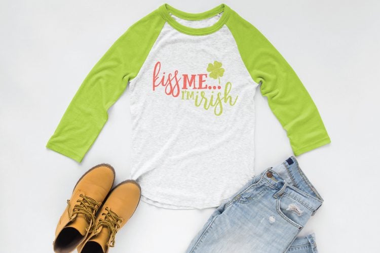A pair of boots, blue jeans and a baseball style shirt with lime green sleeves and decorated on the body of the shirt with a shamrock and the saying, \"Kiss Me.....I\'m Irish\"