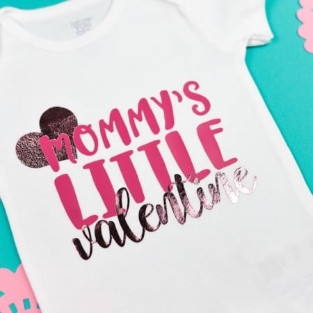 A white onesie decorated with a little heart and the saying, "Mommy's Litte Valentine"