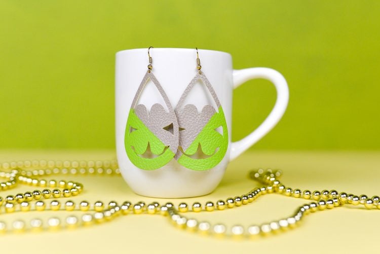 A coffee cup on a table, with Shamrock shaped earrings hanging from it and gold beads next to it