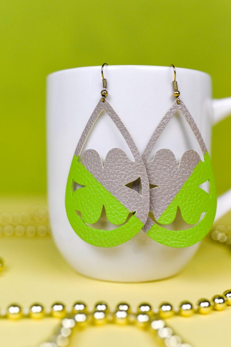 A close up of a coffee cup on a table, with Shamrock shaped earrings hanging from it and gold beads next to it
